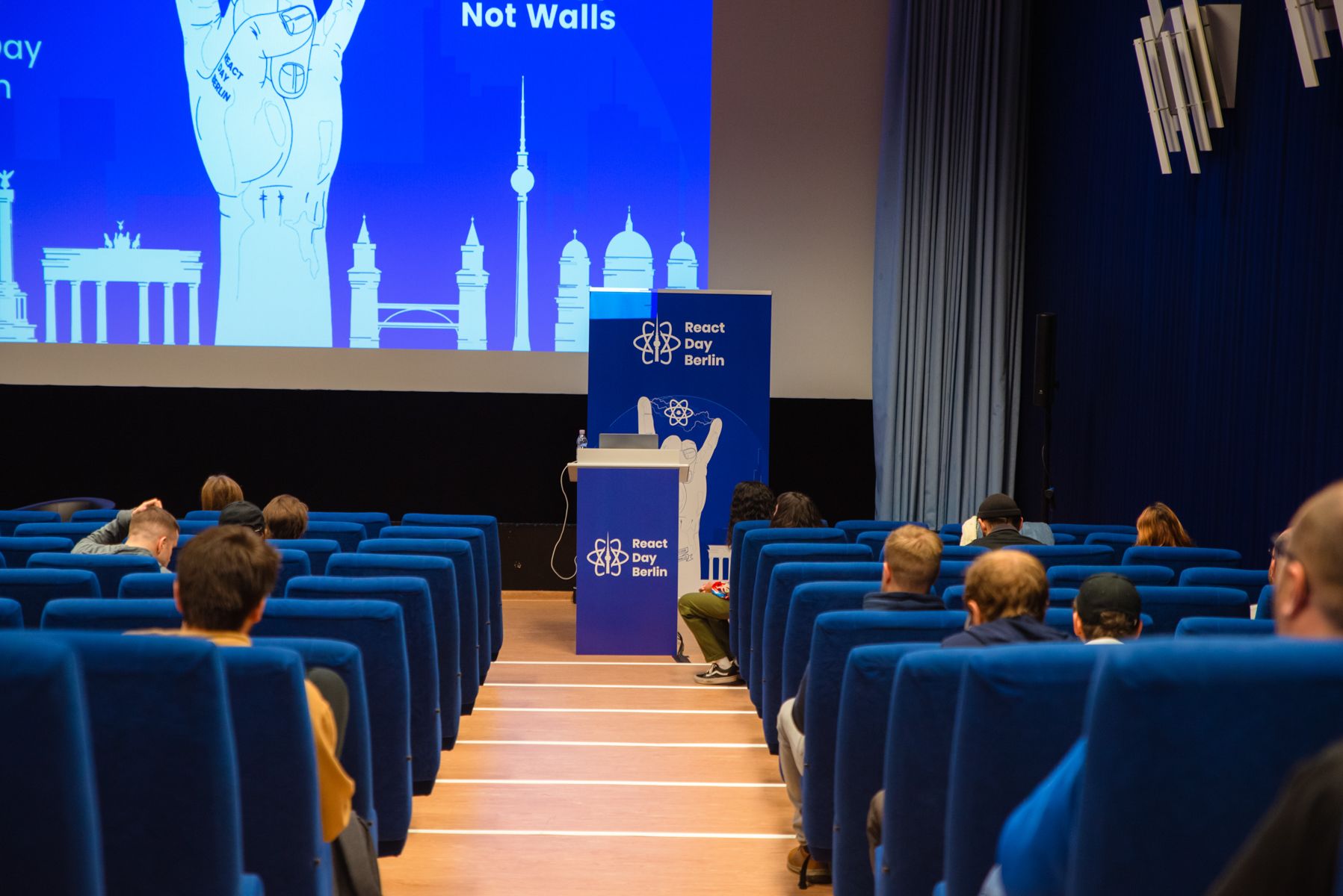 Salle avec plusieurs sièges bleus et une scène avec le logo React Day Berlin