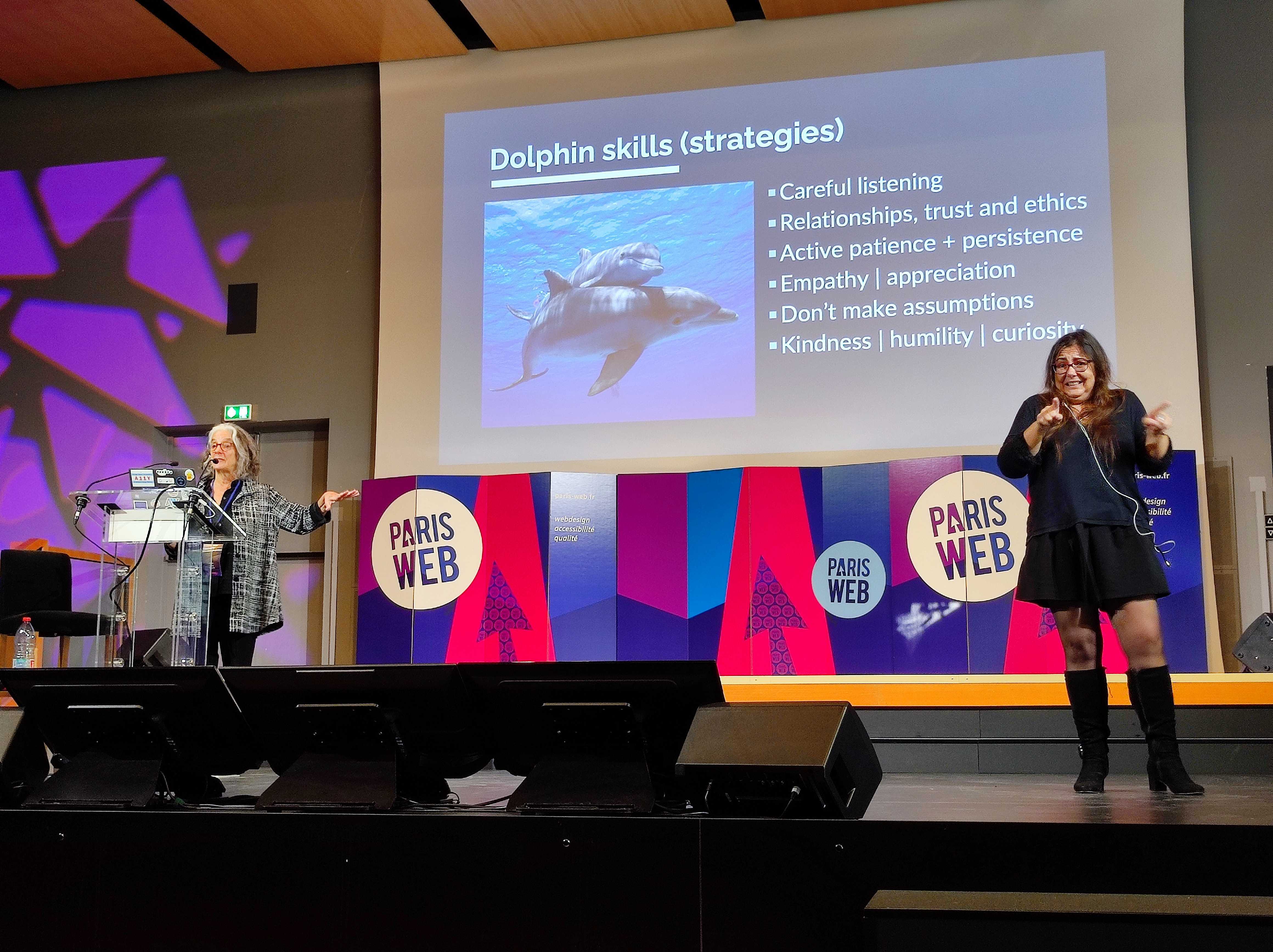 Lainey Feingold pendant sa conférence "Be a Dolphin not a Shark: Using cooperation over conflict to advance digital accessibility". Une interprète LSF est à sa gauche.