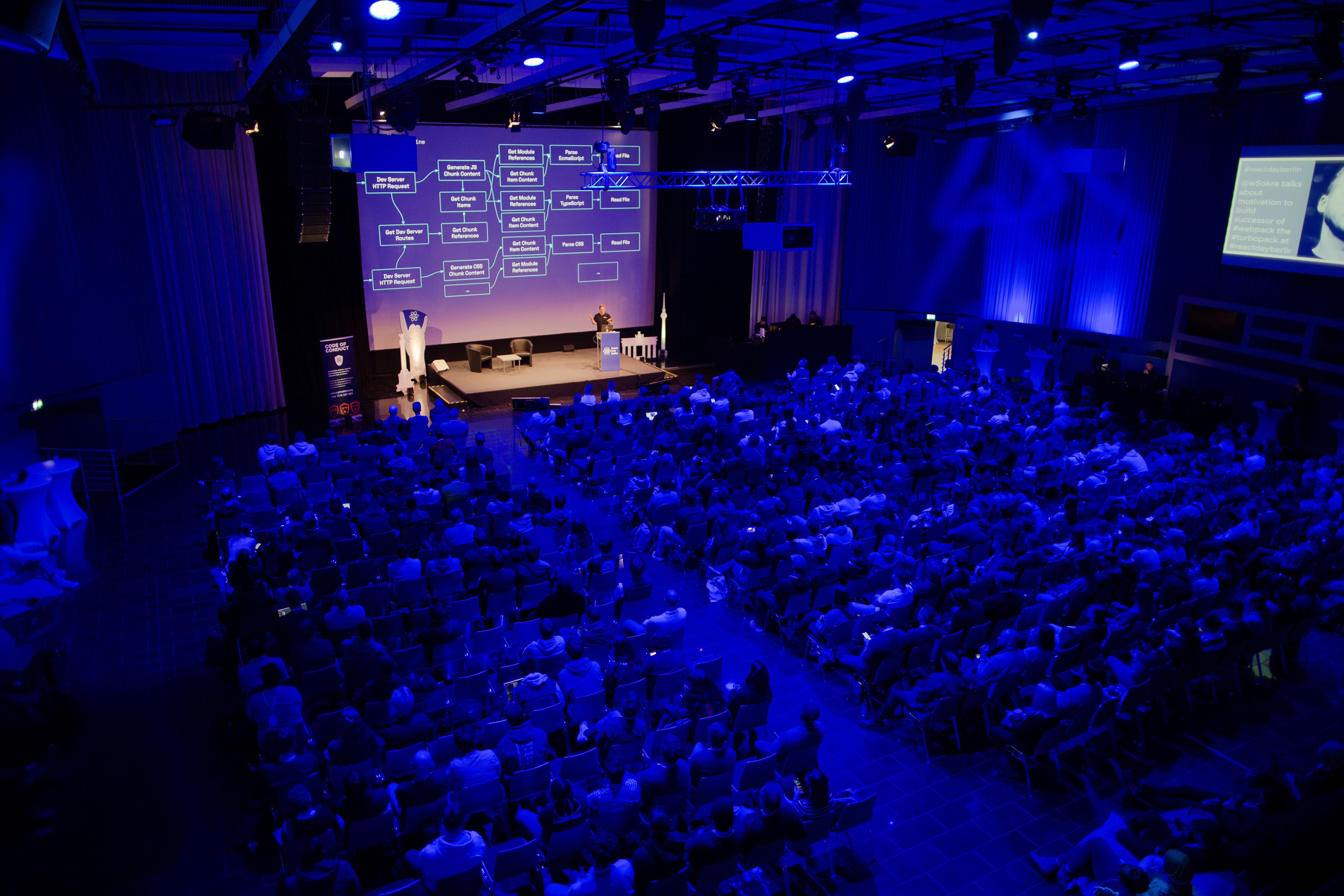 Salle pleine illuminée de lumière bleue et le présentateur sur scène.